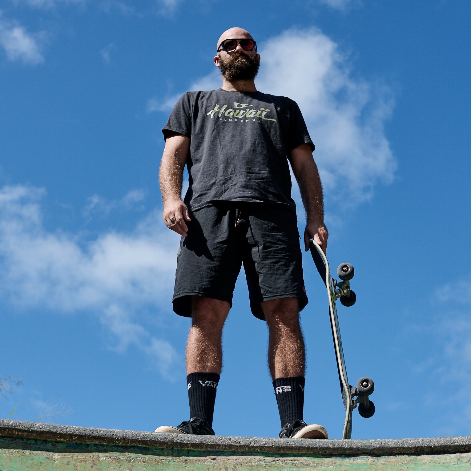 Man holding a skateboard against a blue sky