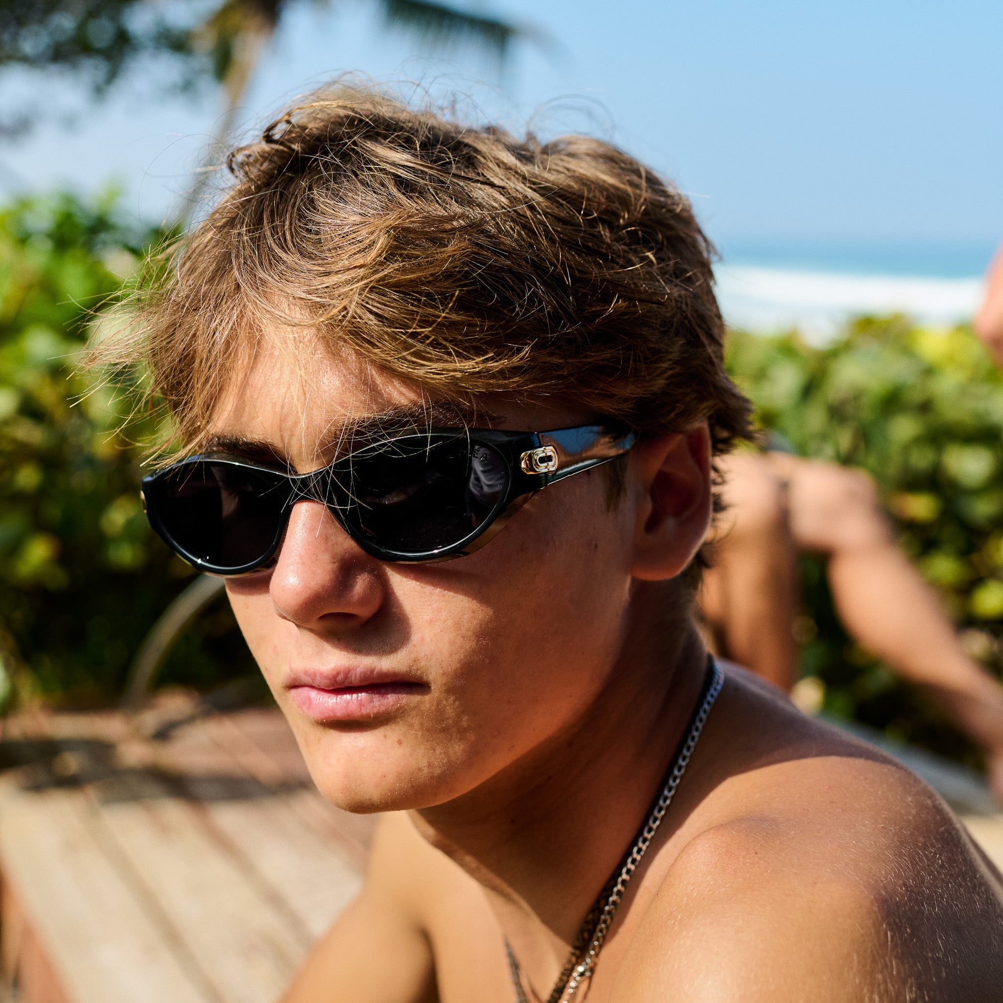 Person wearing sunglasses with a blurred background of greenery and blue sky.
BLACK / SMOKE POLARIZED LENS
