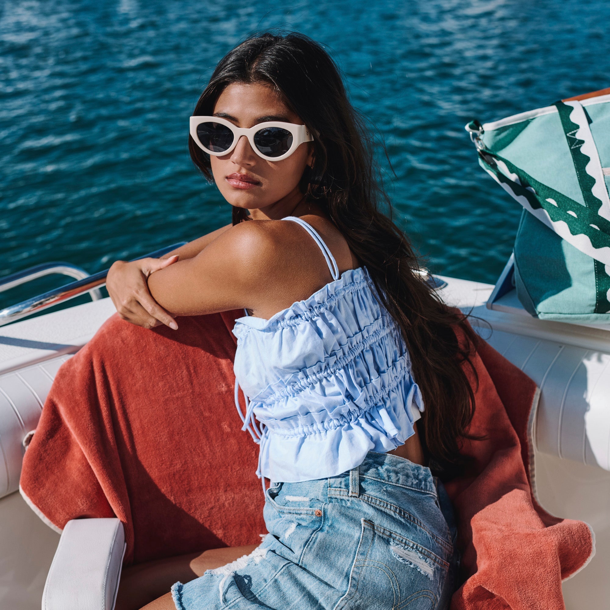 Woman sitting on a boat wearing sunglasses and a blue outfit with a red towel.
CREAM / NAVY POLARIZED LENS