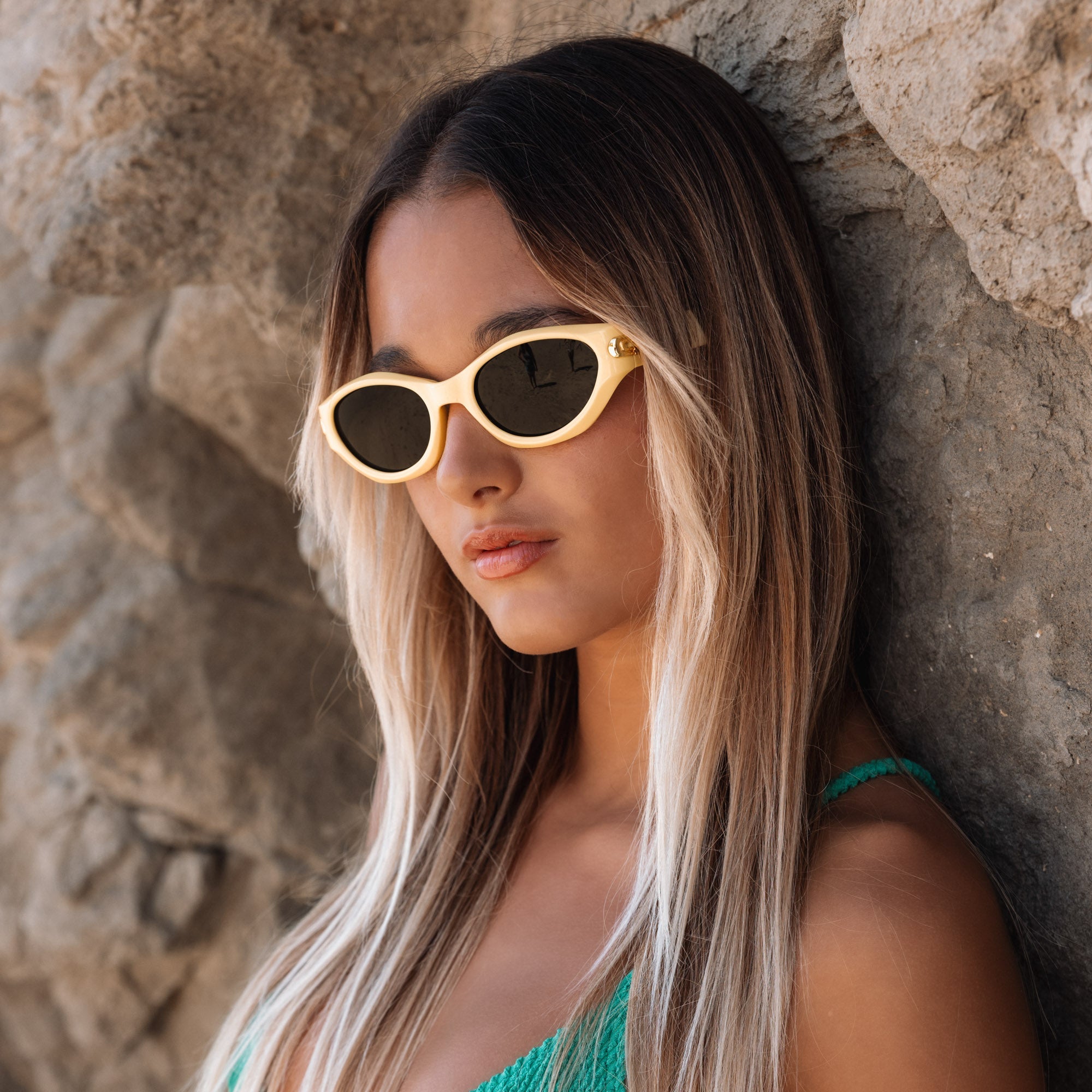 Woman wearing gold sunglasses and a green top against a stone wall.
LEMONADE / SMOKE POLARIZED LENS