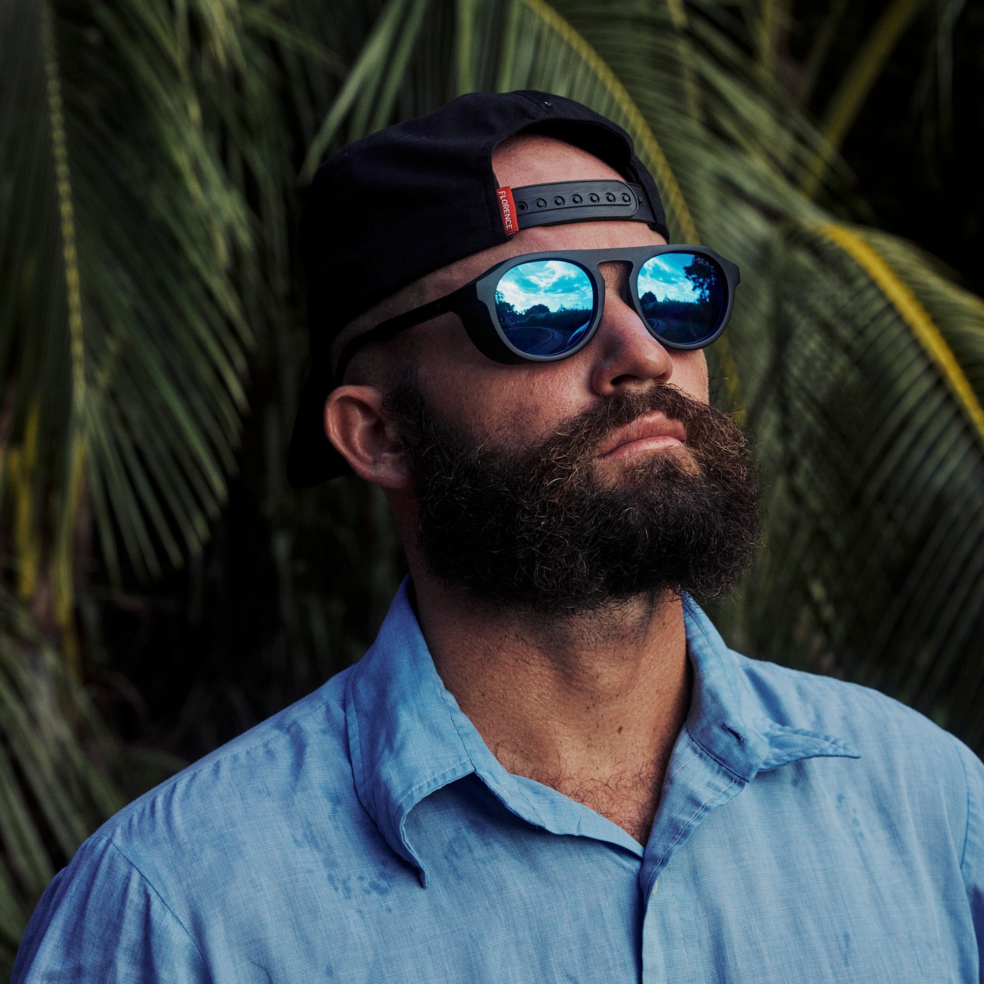 Man wearing sunglasses and a cap with palm leaves in the background