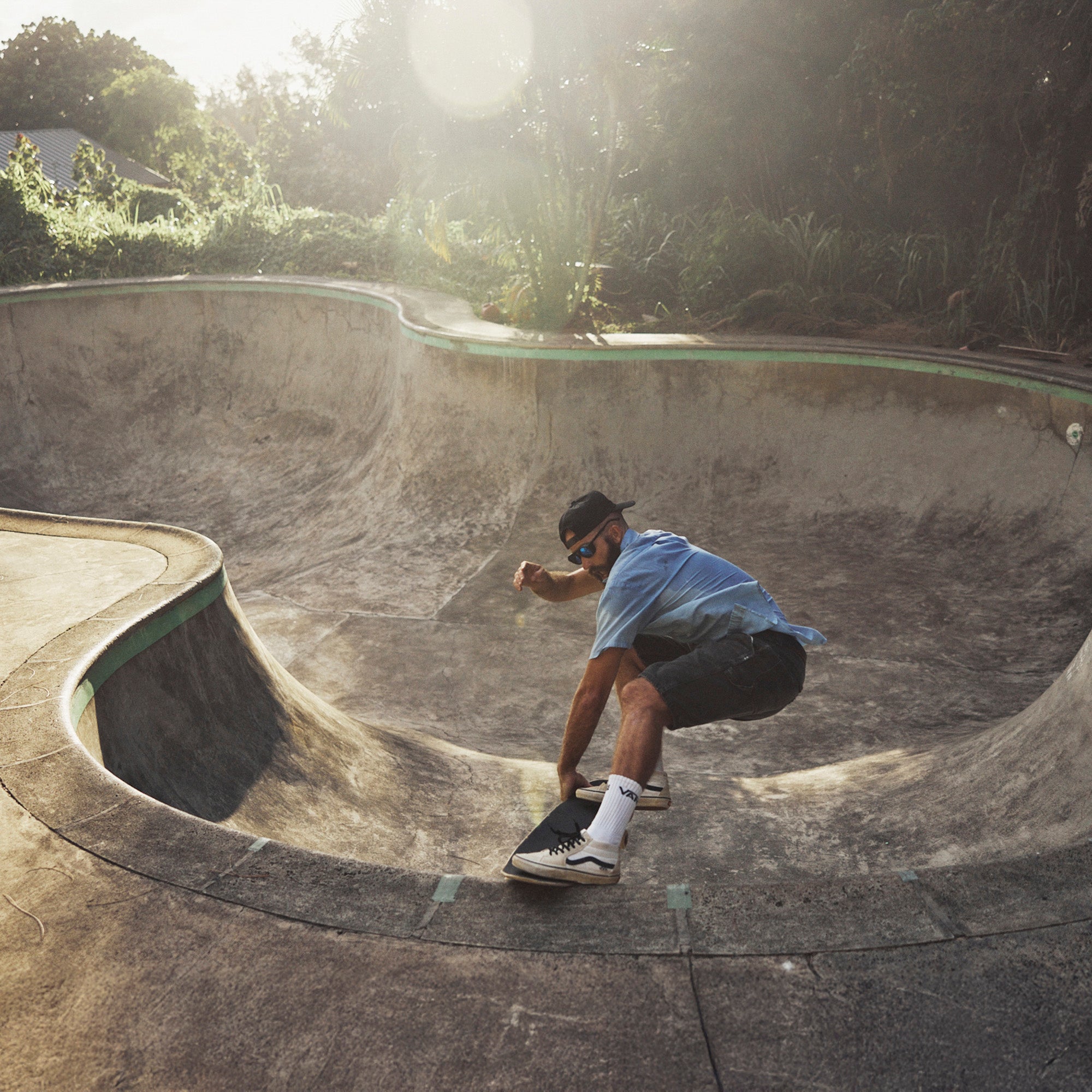 Skateboarder performing a trick in an empty pool with greenery in the background