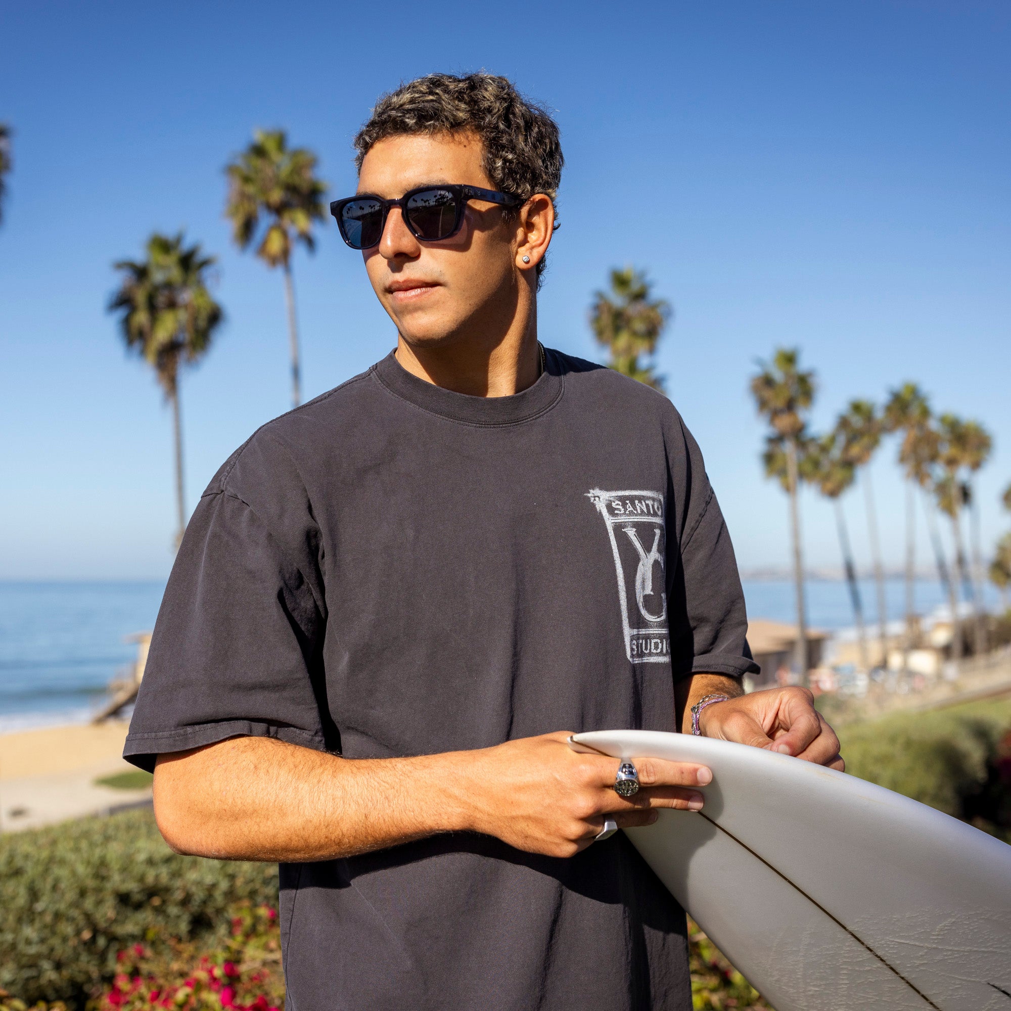 Man holding a surfboard with palm trees and ocean in the background.
DARK SEAS / SMOKE POLARIZED LENS