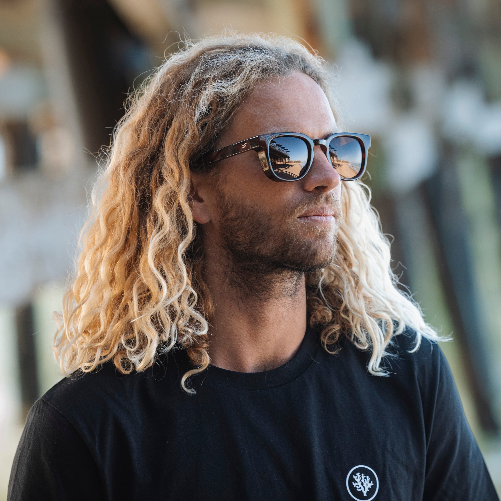 Man with long blonde hair wearing sunglasses and a black t-shirt with a logo.
GREY / NAVY POLARIZED LENS