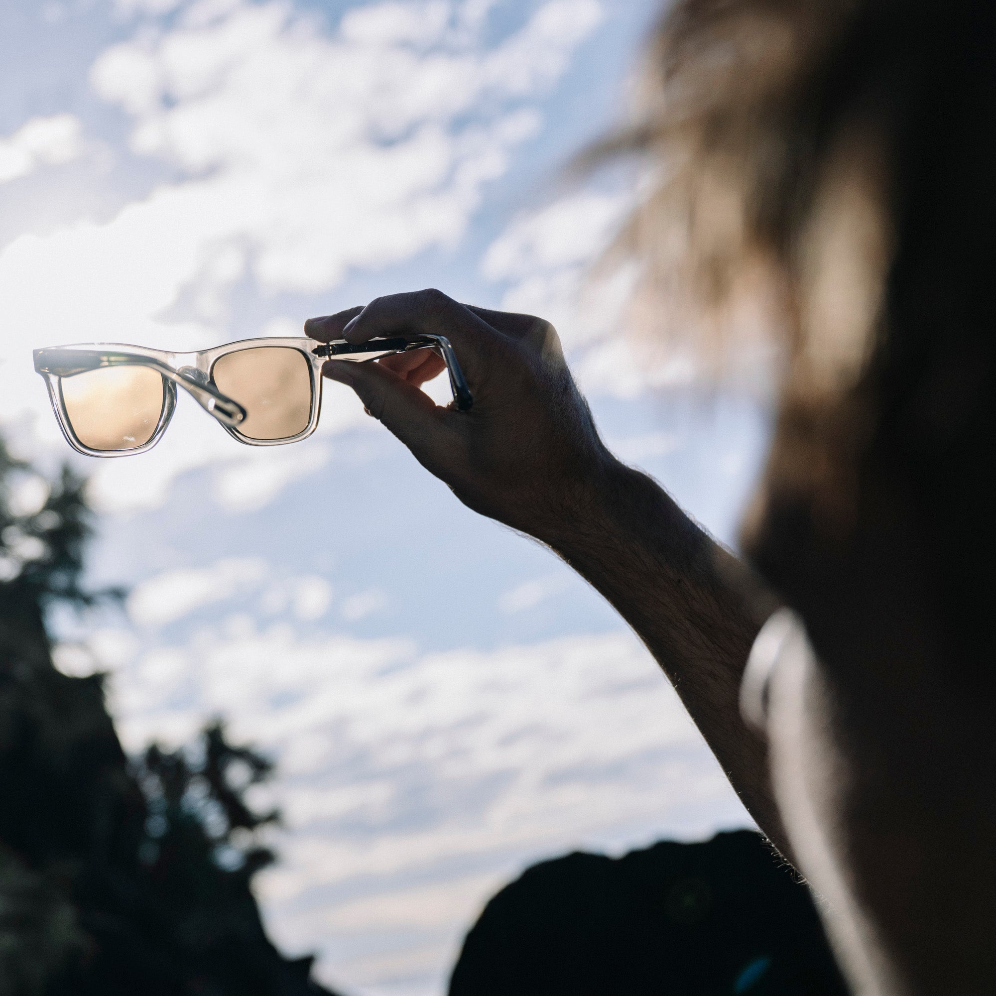 Person holding sunglasses with a blurred natural background.
TAUPE / BROWN POLARIZED LENS