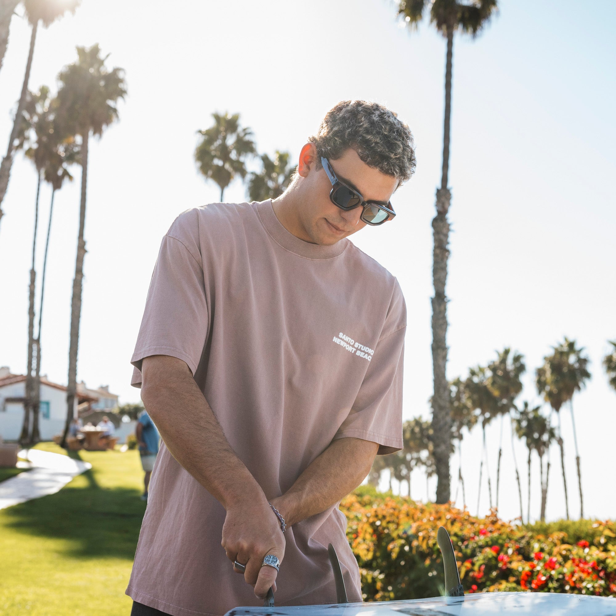 Man wearing sunglasses and a brown t-shirt standing outdoors with palm trees in the background.
TORT / GREEN POLARIZED LENS