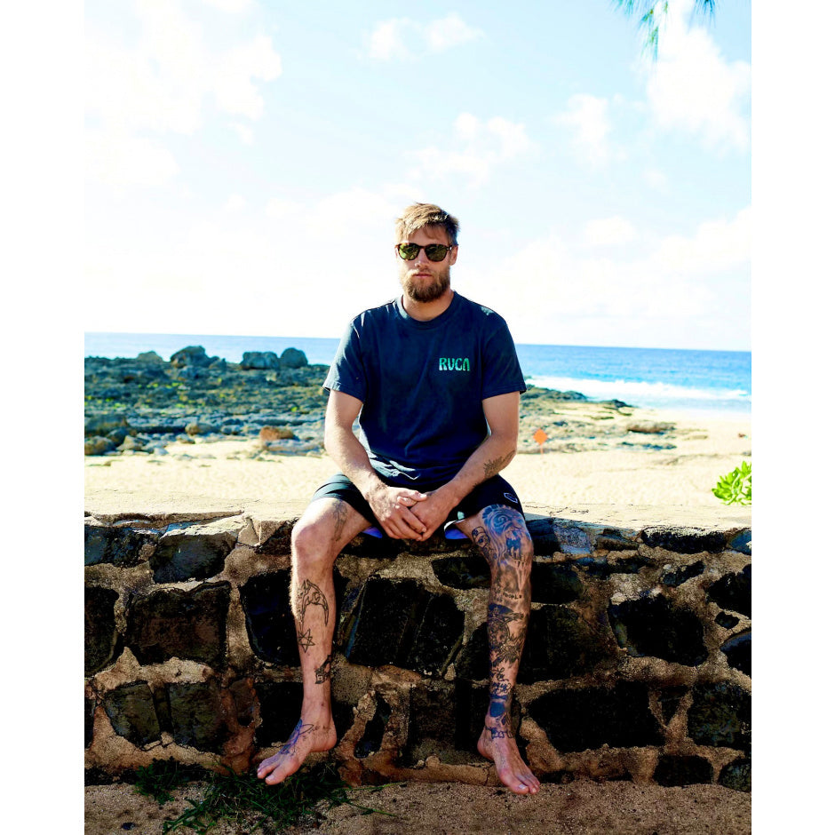 Man sitting on a stone wall by the beach wearing sunglasses and a blue t-shirt.
TORT / BROWN POLARIZED LENS