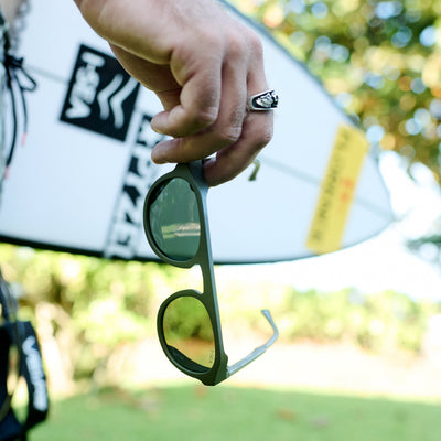Person holding a pair of sunglasses with a blurred outdoor background