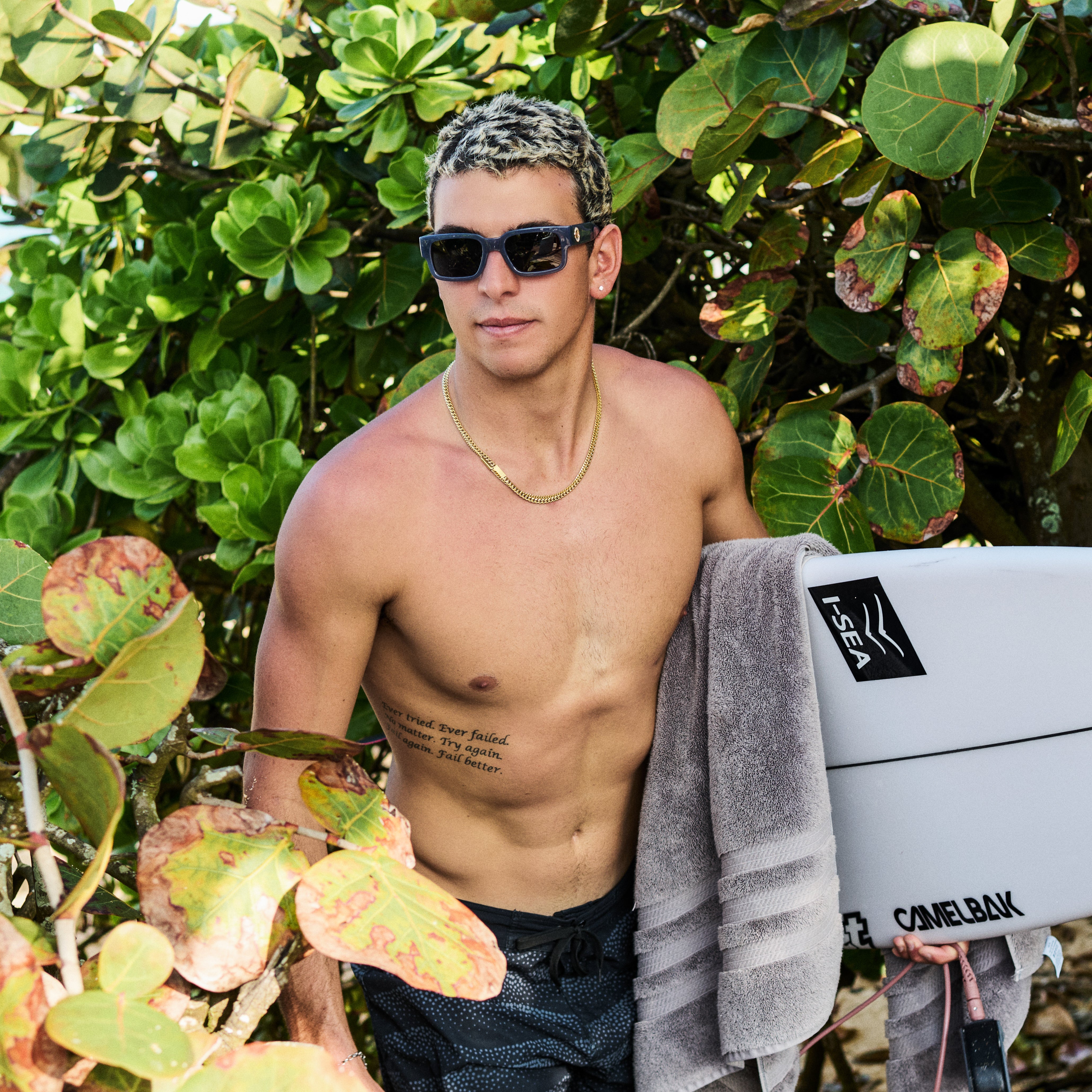 Man with a towel and surfboard standing among green foliage.
GREY / SMOKE POLARIZED LENS