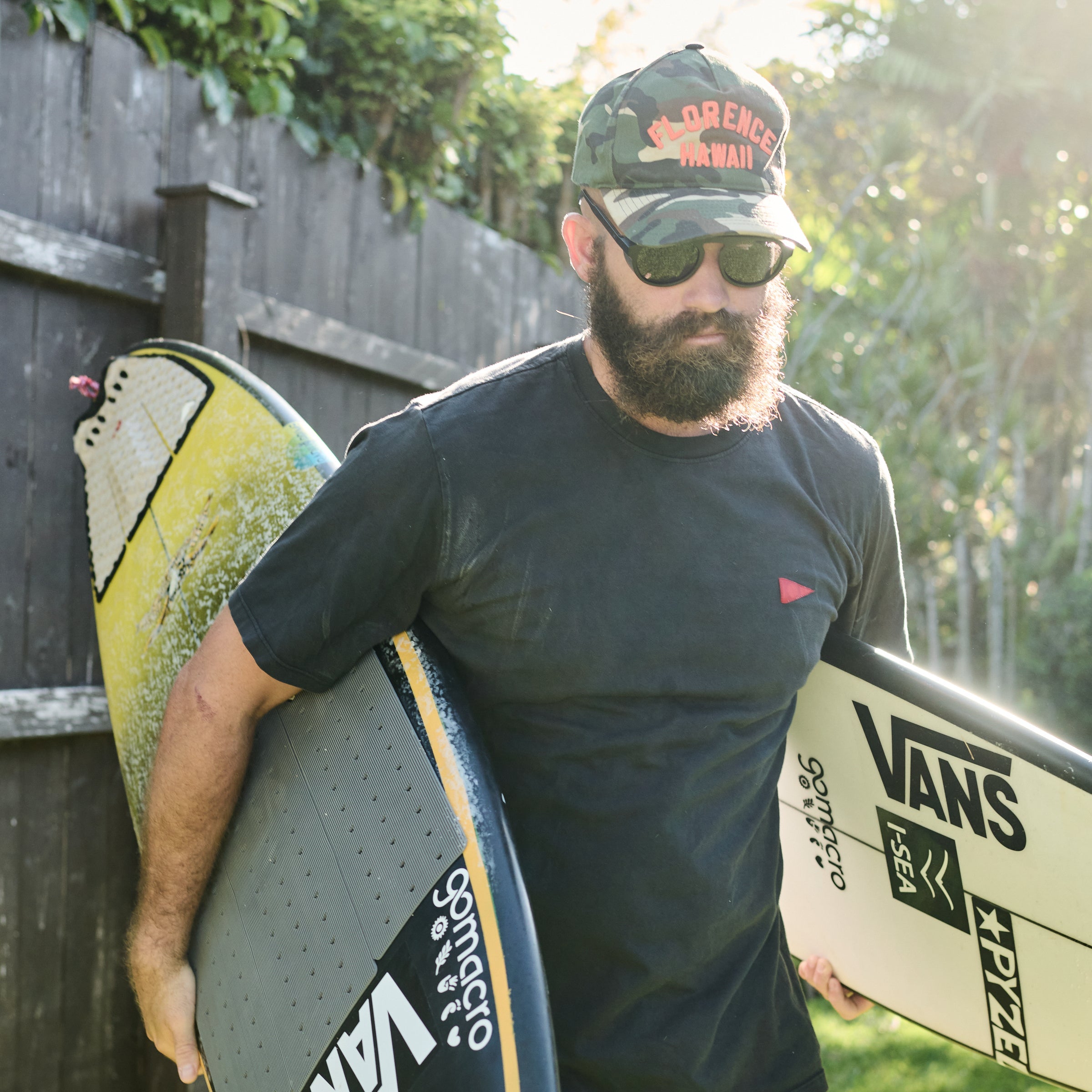 Man holding two surfboards, one with visible branding, against a natural background.