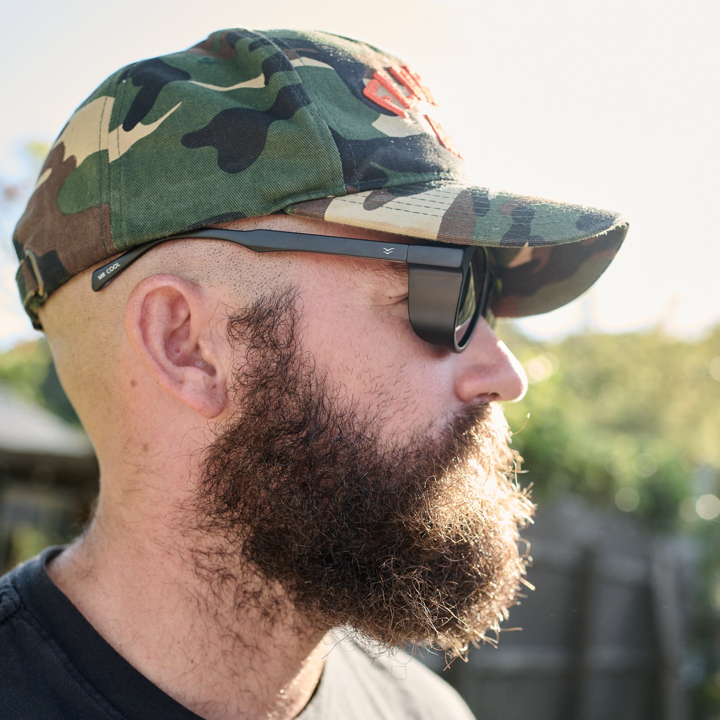 Man wearing a camouflage cap and sunglasses with a blurred natural background