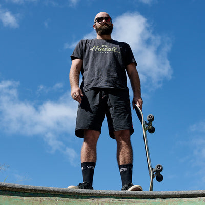 Man holding a skateboard against a blue sky