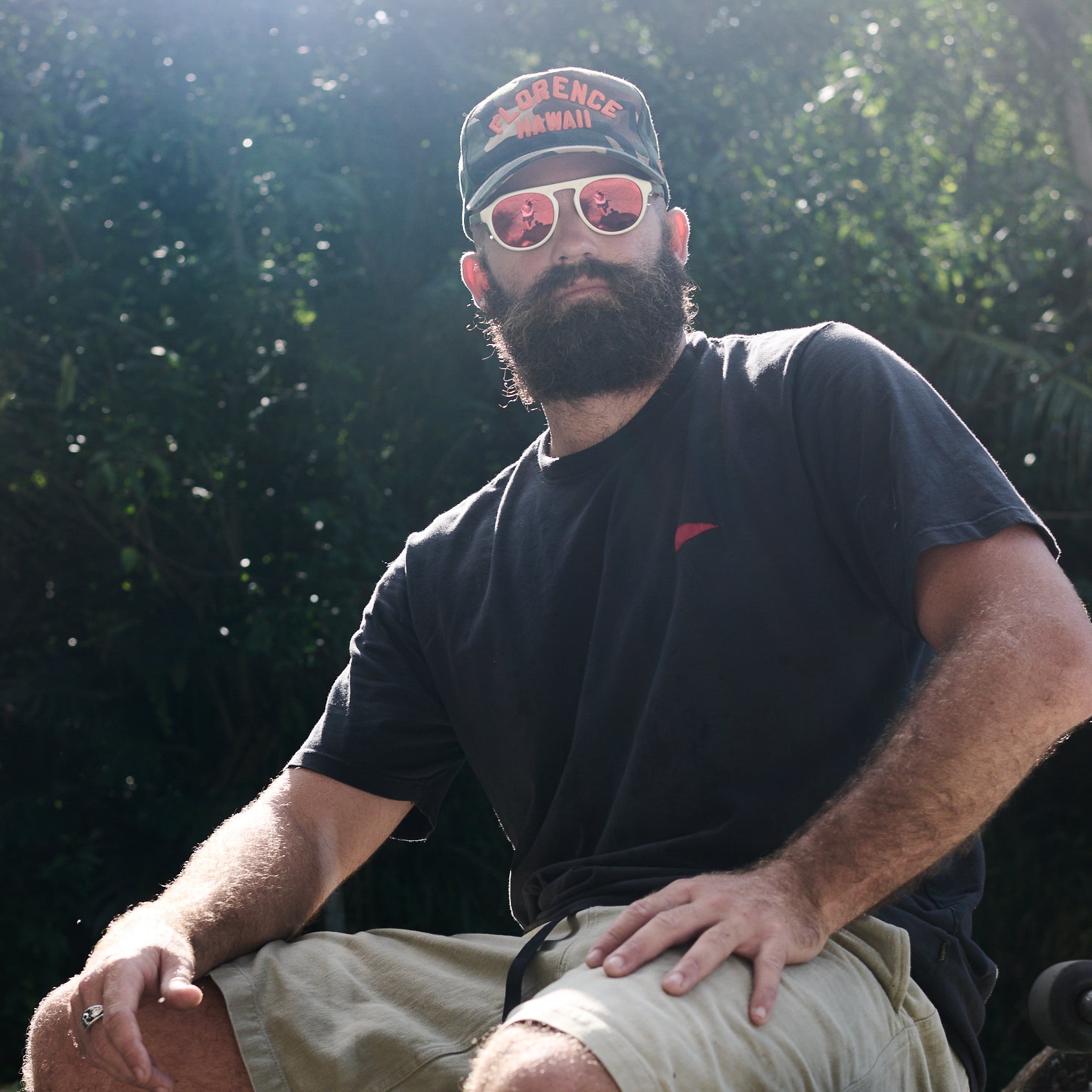 Man wearing a black t-shirt, beige shorts, and a cap with sunglasses outdoors.