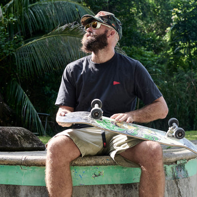 Man sitting on a ledge with a skateboard, surrounded by greenery