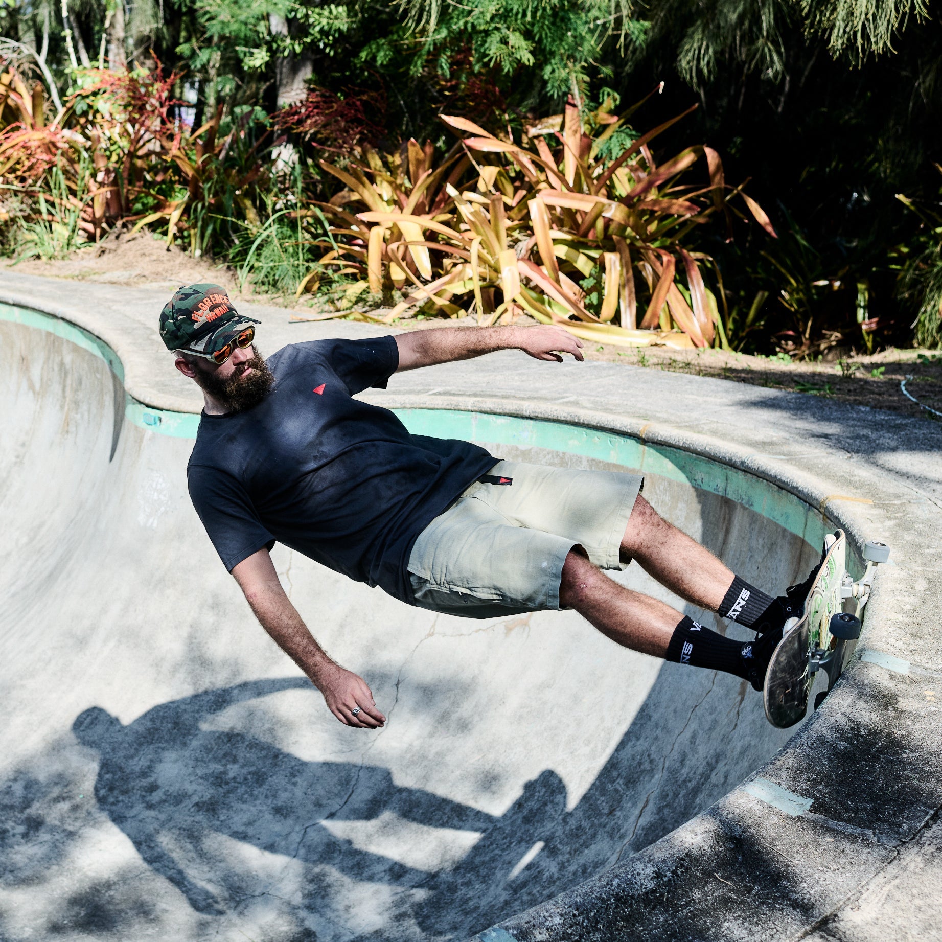 Person skateboarding in a concrete bowl with plants in the background