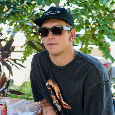 Man wearing sunglasses and a cap with plants in the background.
TAUPE / BROWN POLARIZED LENS