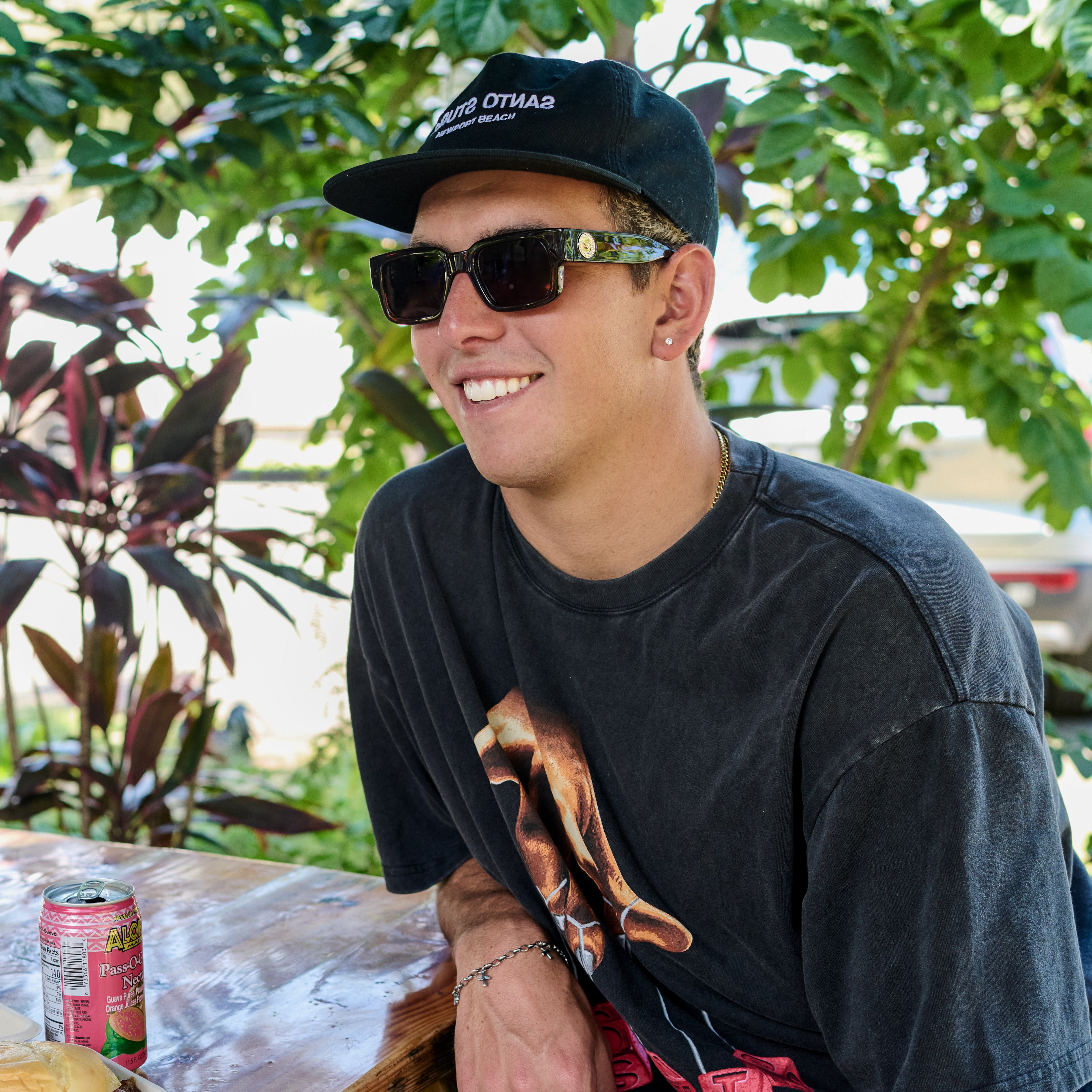 Person wearing sunglasses and a cap, sitting outdoors with plants in the background.
TAUPE / BROWN POLARIZED LENS