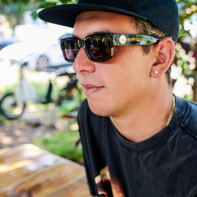Person wearing sunglasses and a cap outdoors with blurred background.
TAUPE / BROWN POLARIZED LENS