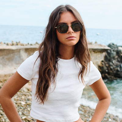 Woman wearing sunglasses and a white t-shirt by the sea. Color:
EMERALD / GREEN POLARIZED LENS
