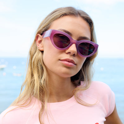 Woman wearing purple sunglasses with a blurred beach background.
ROSE / PLUM POLARIZED LENS