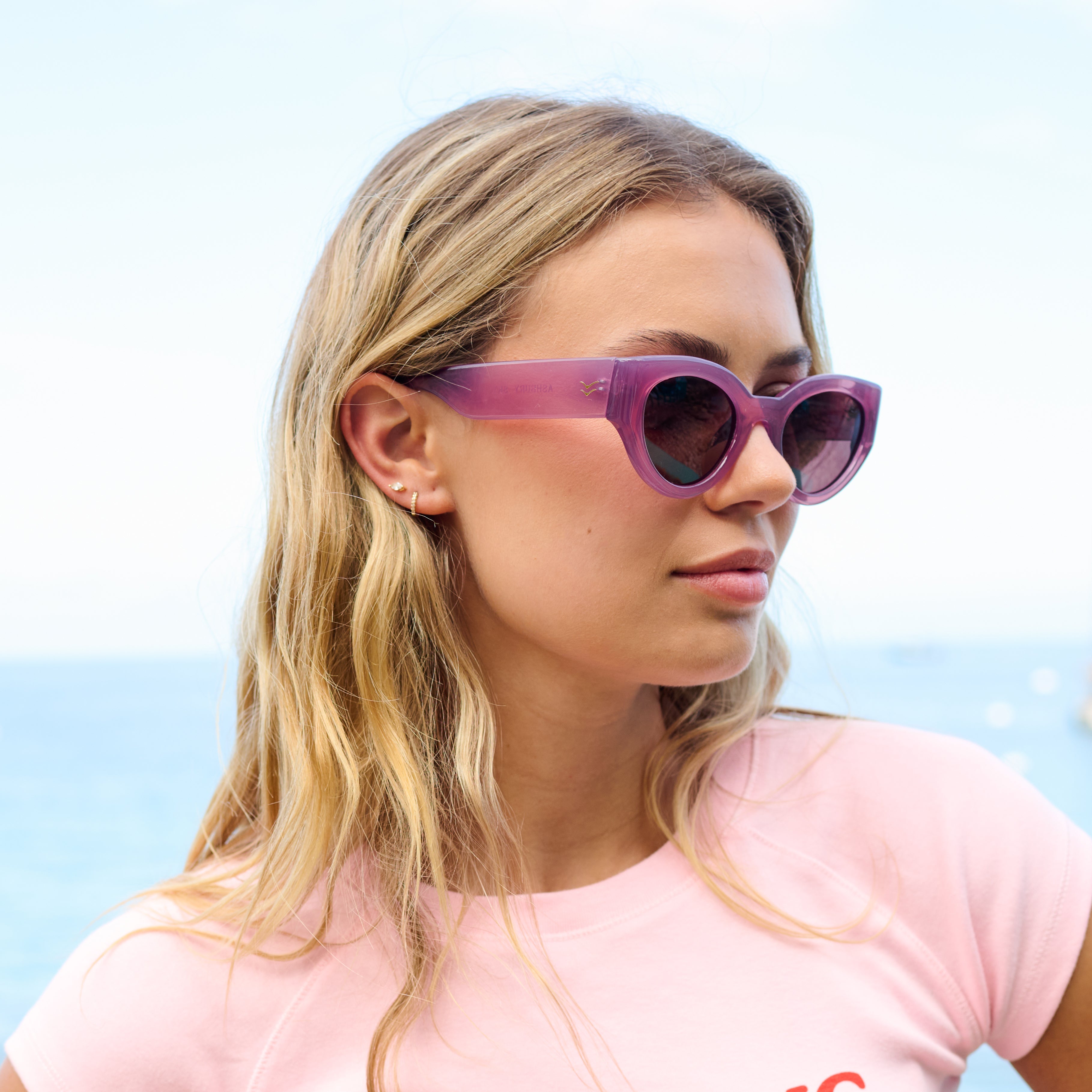 Woman wearing purple sunglasses with a blurred beach background.
ROSE / PLUM POLARIZED LENS