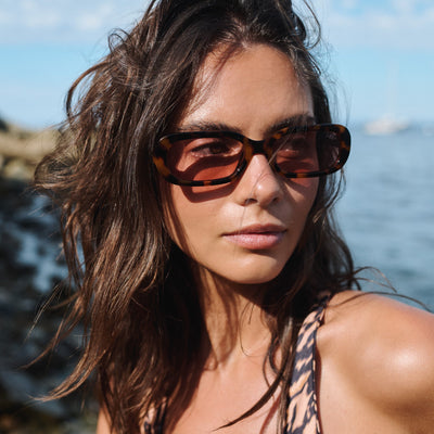 Woman wearing sunglasses with a blurred background of water and sky.
TORT / PEACH POLARIZED LENS