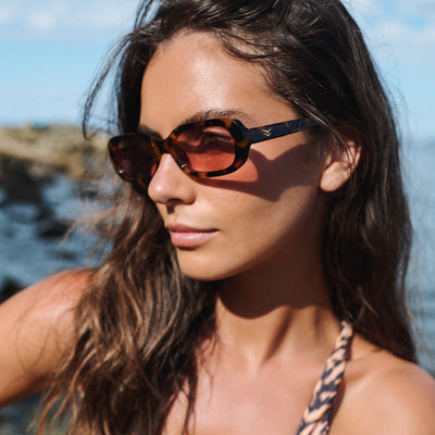 Woman wearing sunglasses with a blurred natural background.
TORT / PEACH POLARIZED LENS