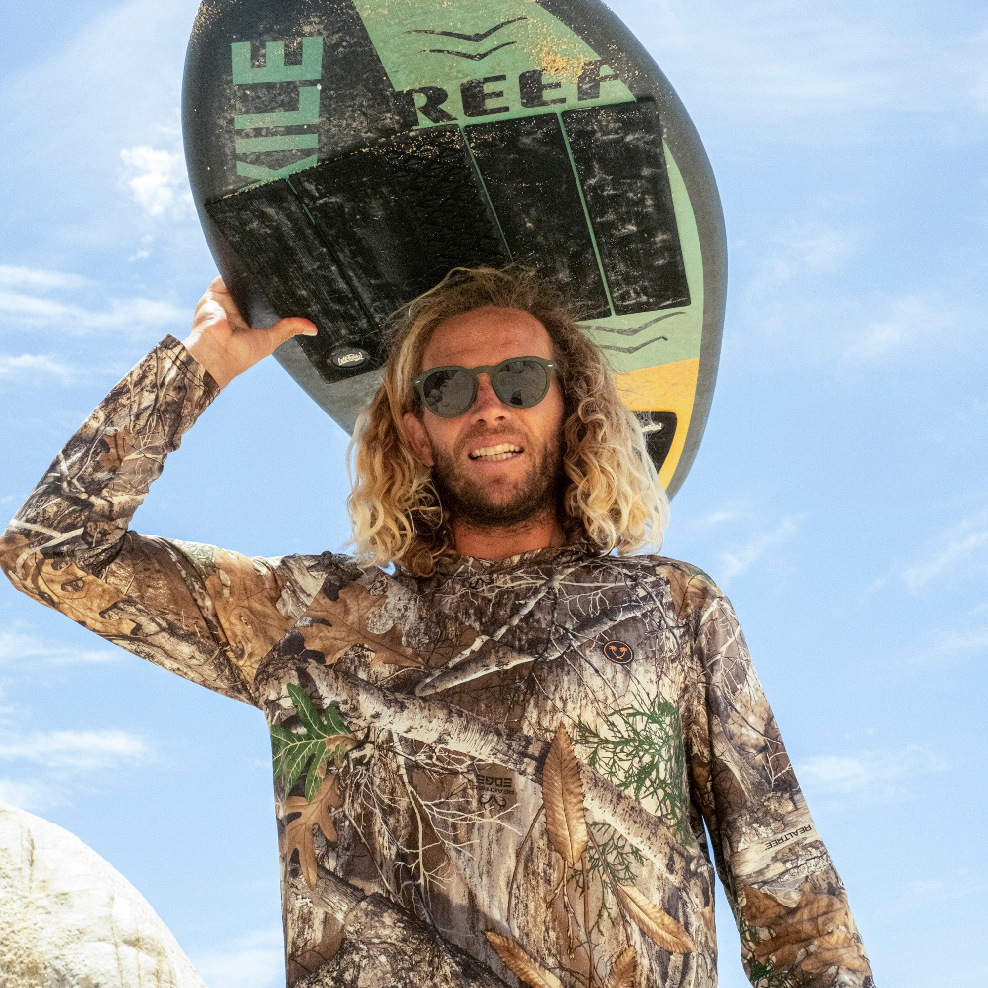 Man holding a surfboard with 'Reef' branding against a blue sky.
KALE / GREEN POLARIZED LENS