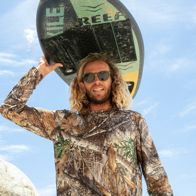 Man holding a surfboard with 'Reef' branding against a blue sky.
KALE / GREEN POLARIZED LENS