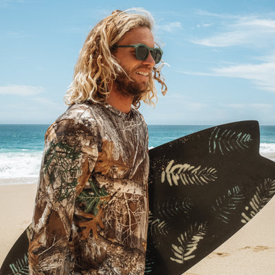 Man with a camouflage shirt holding a surfboard on a beach.
KALE / GREEN POLARIZED LENS