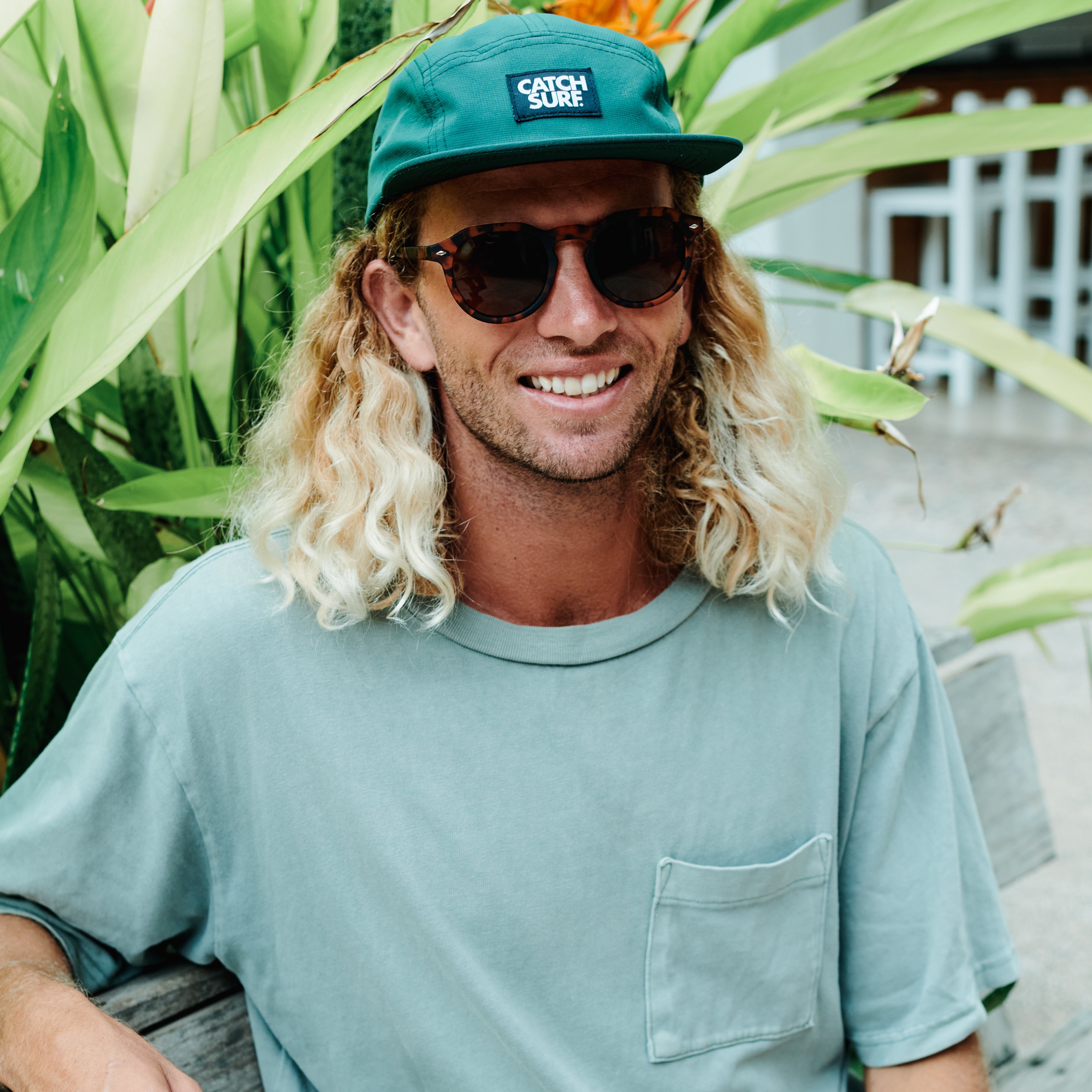 Man wearing a teal cap and sunglasses with plants in the background.
TORT / BROWN POLARIZED LENS