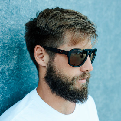 Man with sunglasses and beard against a blue textured wall.
TORT / BROWN POLARIZED LENS