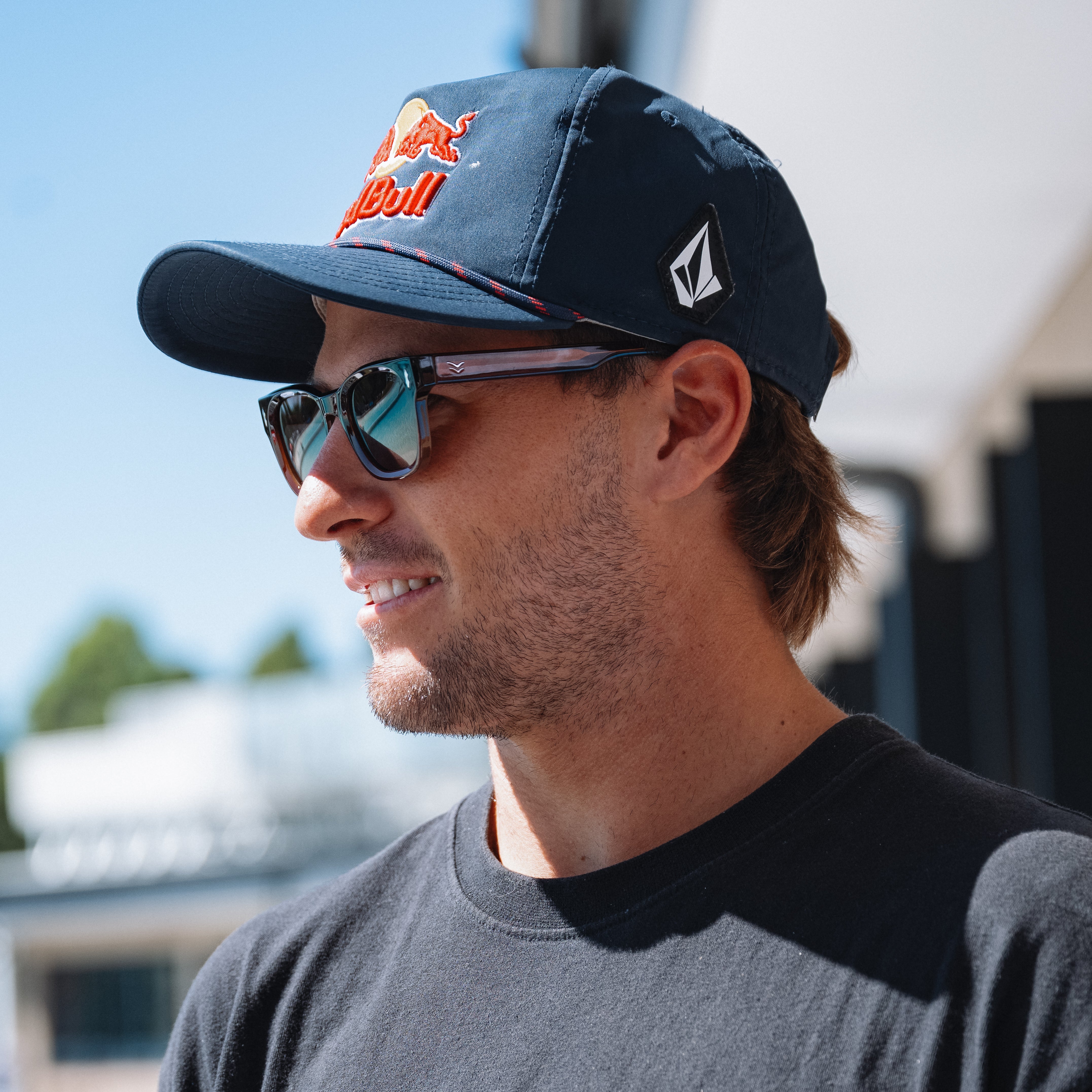 Man wearing a navy cap with a logo and sunglasses, outdoors.
TORT COLA / BROWN POLARIZED LENS
