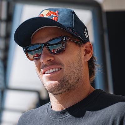 Man wearing a cap with a logo and sunglasses, smiling outdoors.
TORT COLA / BROWN POLARIZED LENS