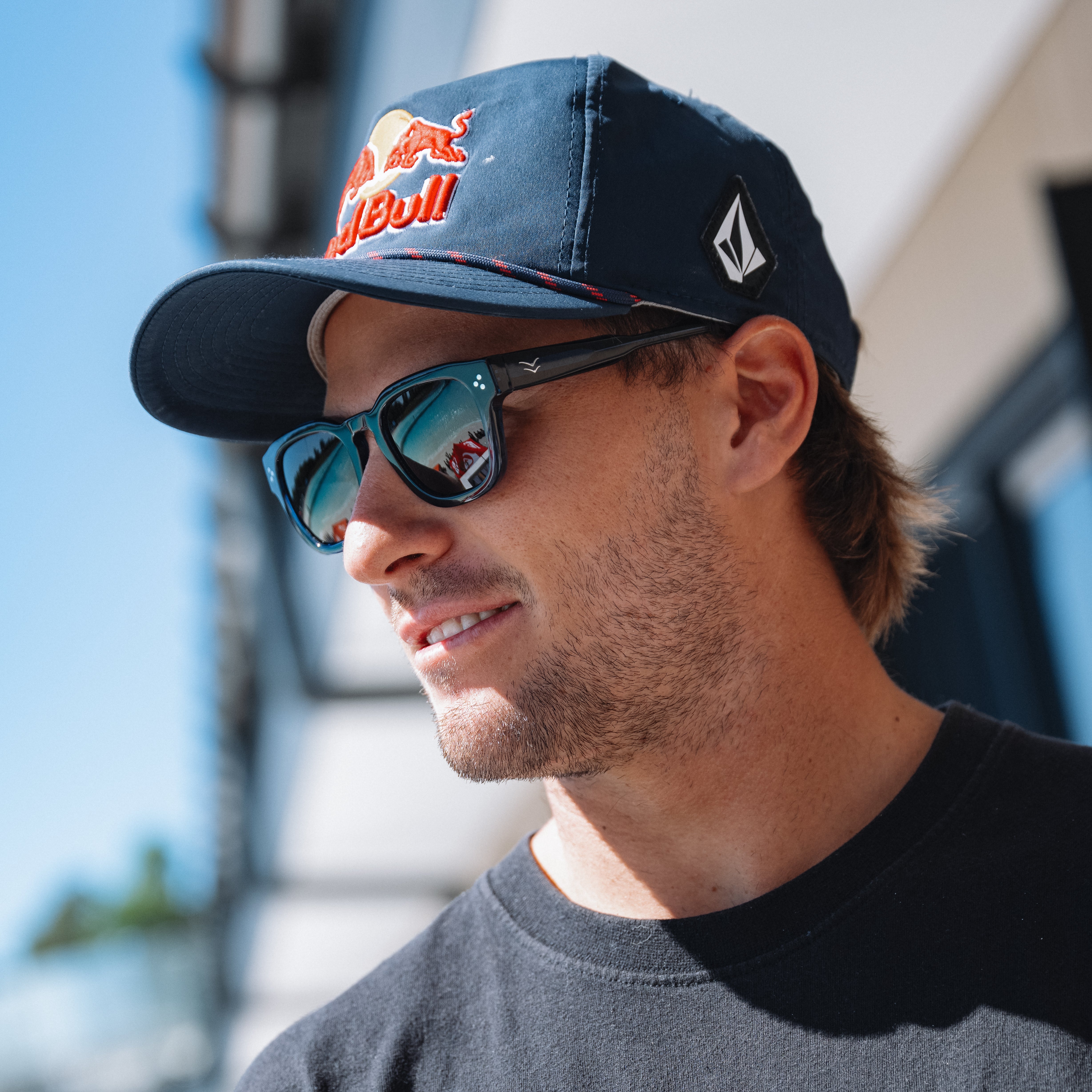 Man wearing a navy cap with a red bull logo and sunglasses, outdoors.
BLACK / GREEN POLARIZED LENS
