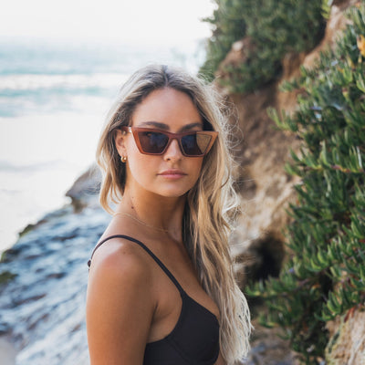 Woman wearing sunglasses and a black top by a scenic coastal area.
COFFEE / BROWN POLARIZED LENS