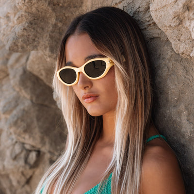 Woman wearing gold sunglasses and a green top against a stone wall.
LEMONADE / SMOKE POLARIZED LENS