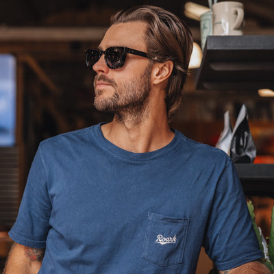 Man wearing sunglasses and a blue t-shirt with a logo, standing in a casual setting.
BLACK / SMOKE POLARIZED LENS