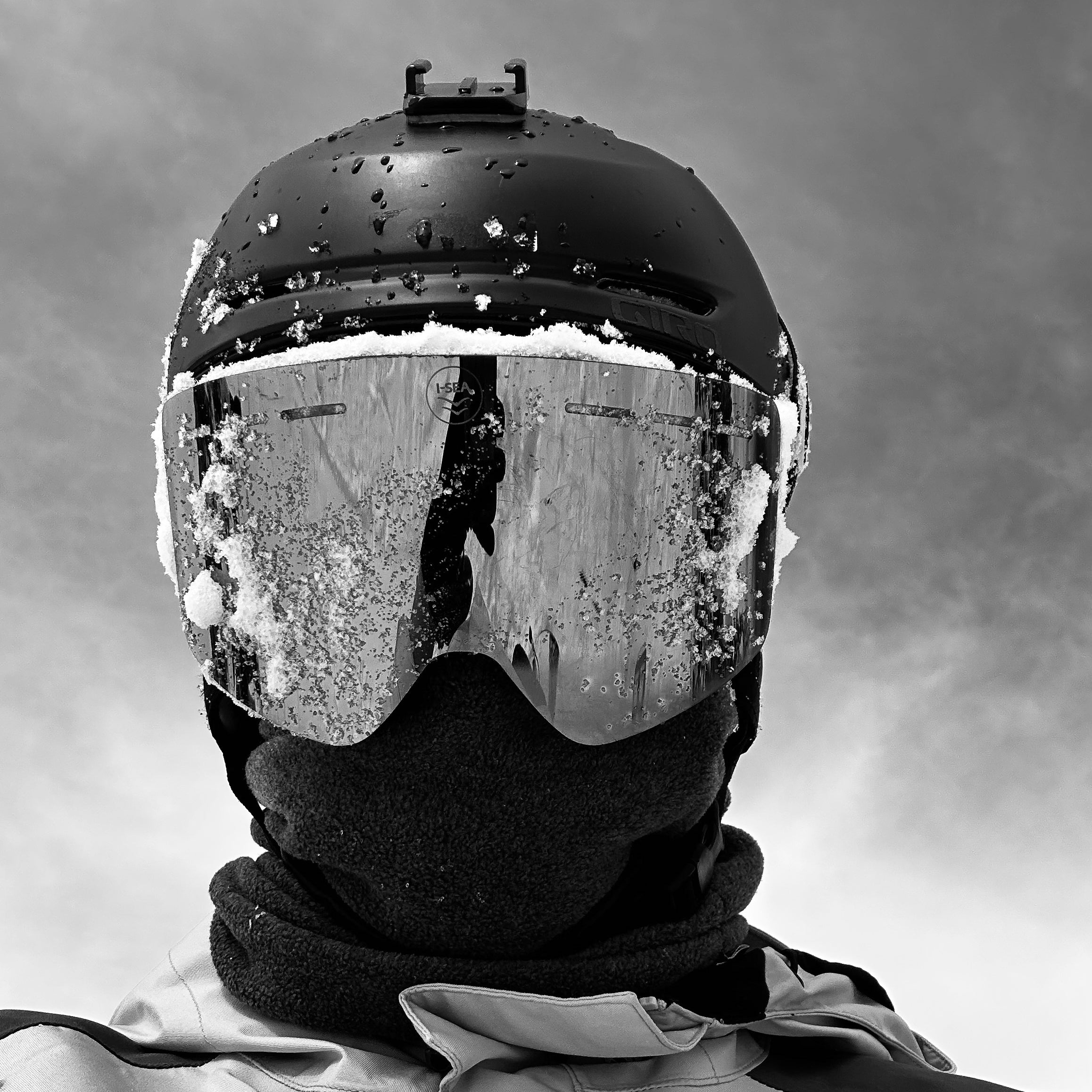 Person wearing a black helmet and goggles with snow on a gray background.
OLIVE / SILVER
