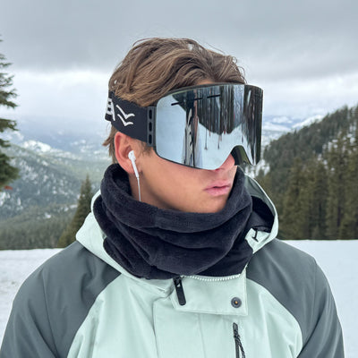Person wearing reflective goggles and a dark scarf in a snowy landscape.
OLIVE / SILVER