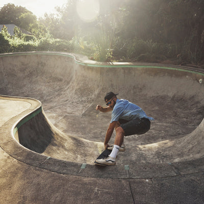 Skateboarder performing a trick in an empty pool with greenery in the background