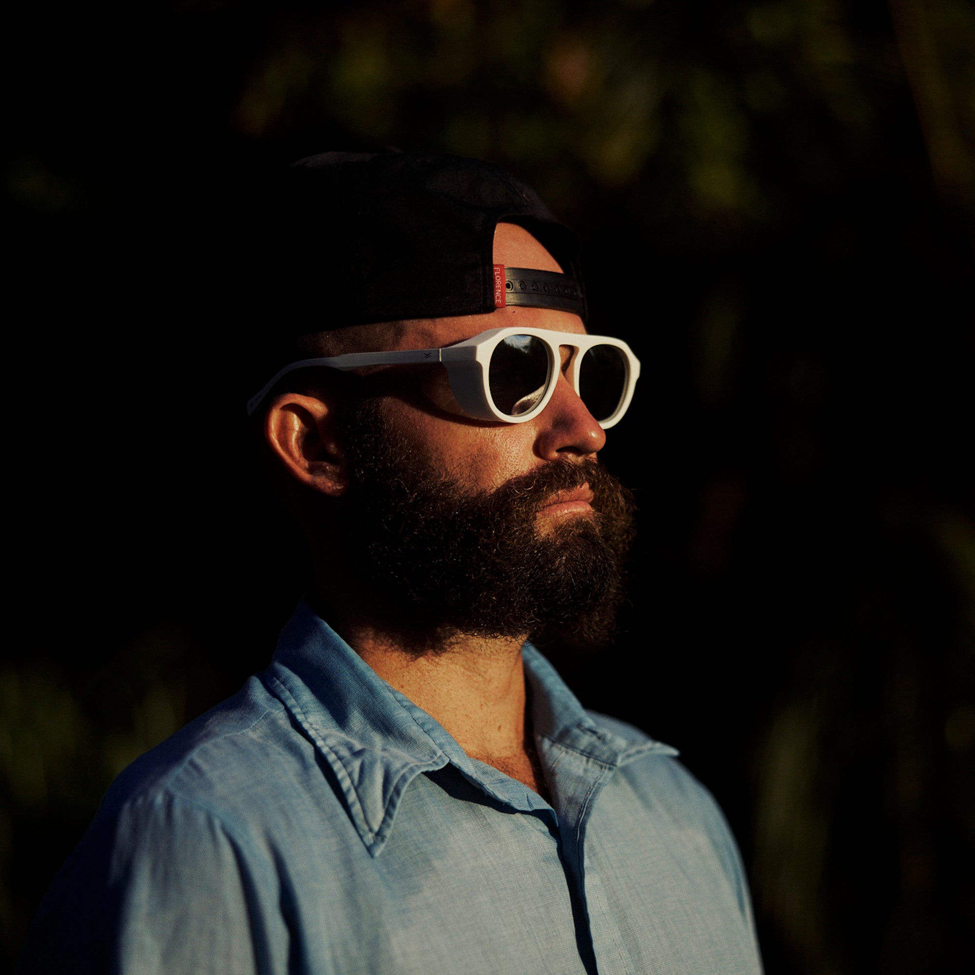 Man wearing a cap and sunglasses with a dark background