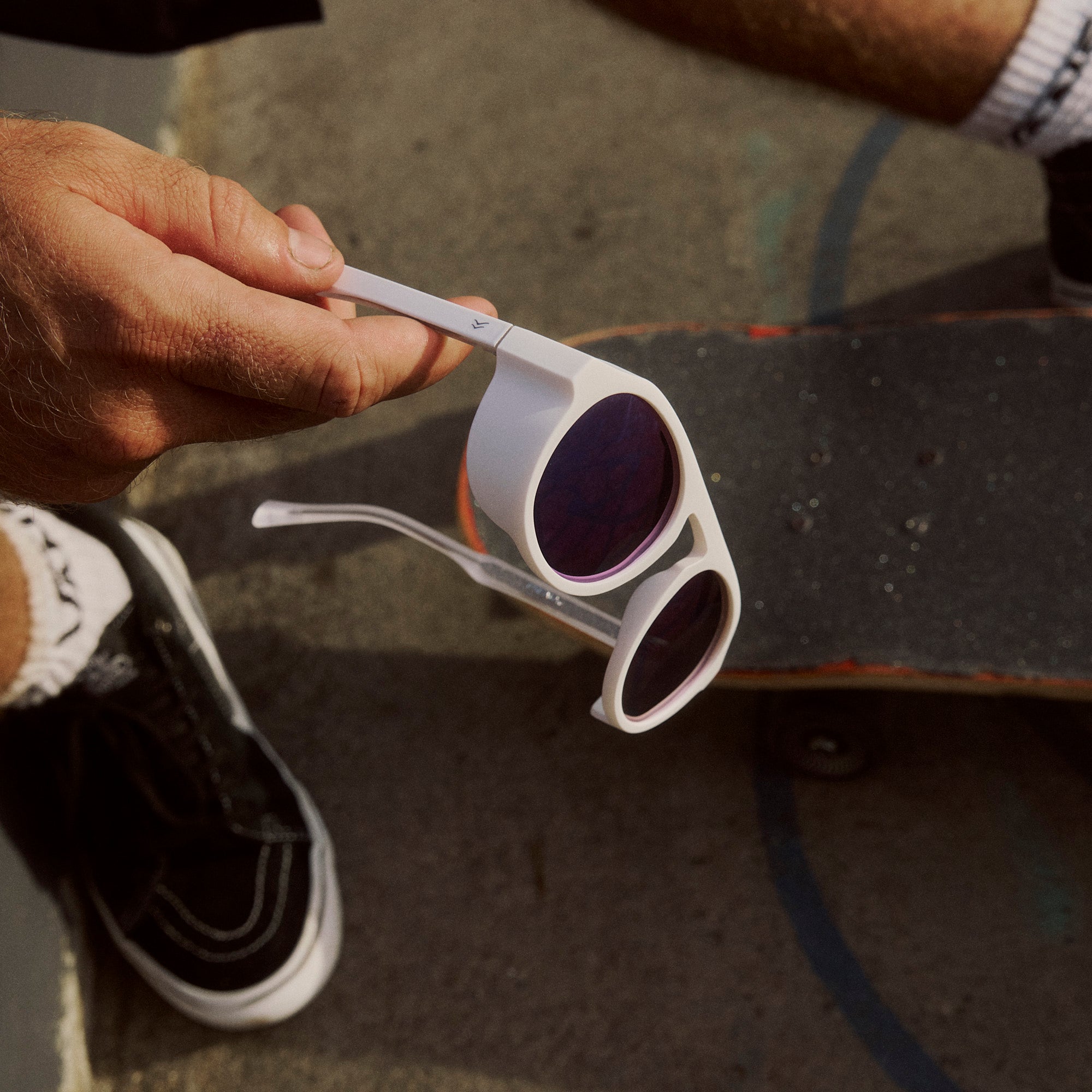 Person holding white sunglasses with purple lenses on a skateboard