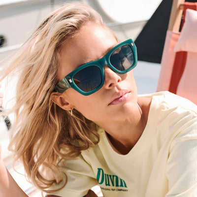 Person wearing teal sunglasses and a light-colored shirt with 'Duvall' branding.
KALE / GREEN POLARIZED LENS