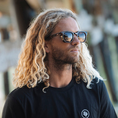 Man with long blonde hair wearing sunglasses and a black t-shirt with a logo.
GREY / NAVY POLARIZED LENS