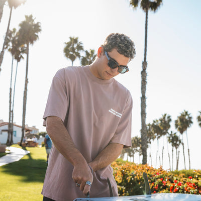 Man wearing sunglasses and a brown t-shirt standing outdoors with palm trees in the background.
TORT / GREEN POLARIZED LENS