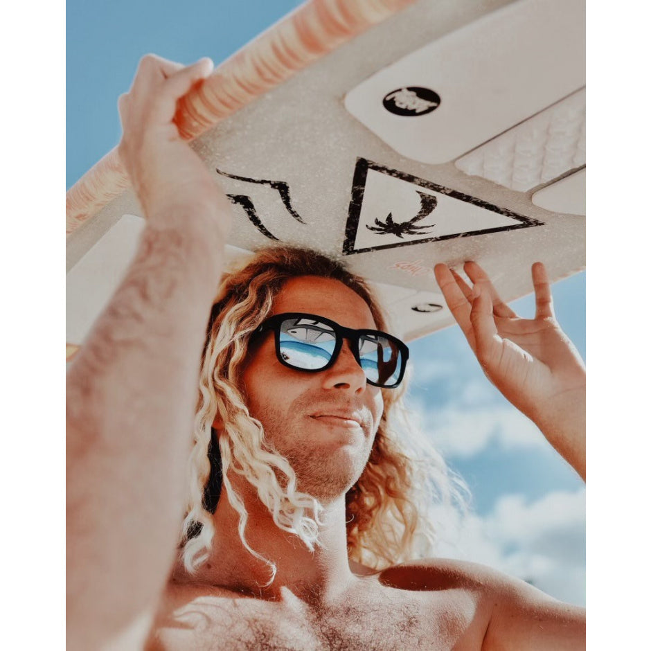 Man holding a surfboard with a blue sky background.
BLACK / T-BLUE POLARIZED LENS