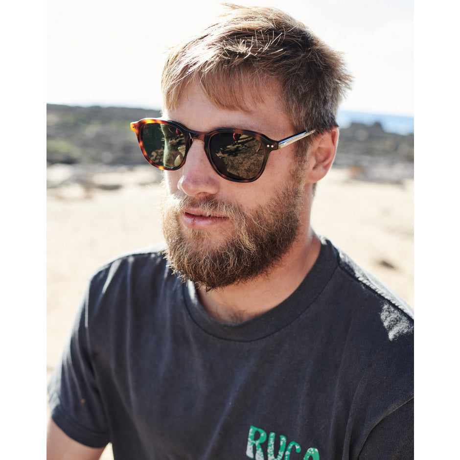 Man wearing sunglasses with a blurred beach background.
TORT / BROWN POLARIZED LENS