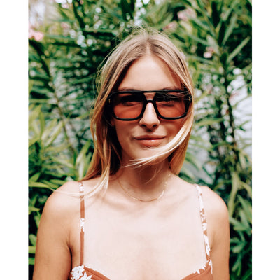 Woman wearing large sunglasses with a green leafy background.
BLACK / PEACH LENS
